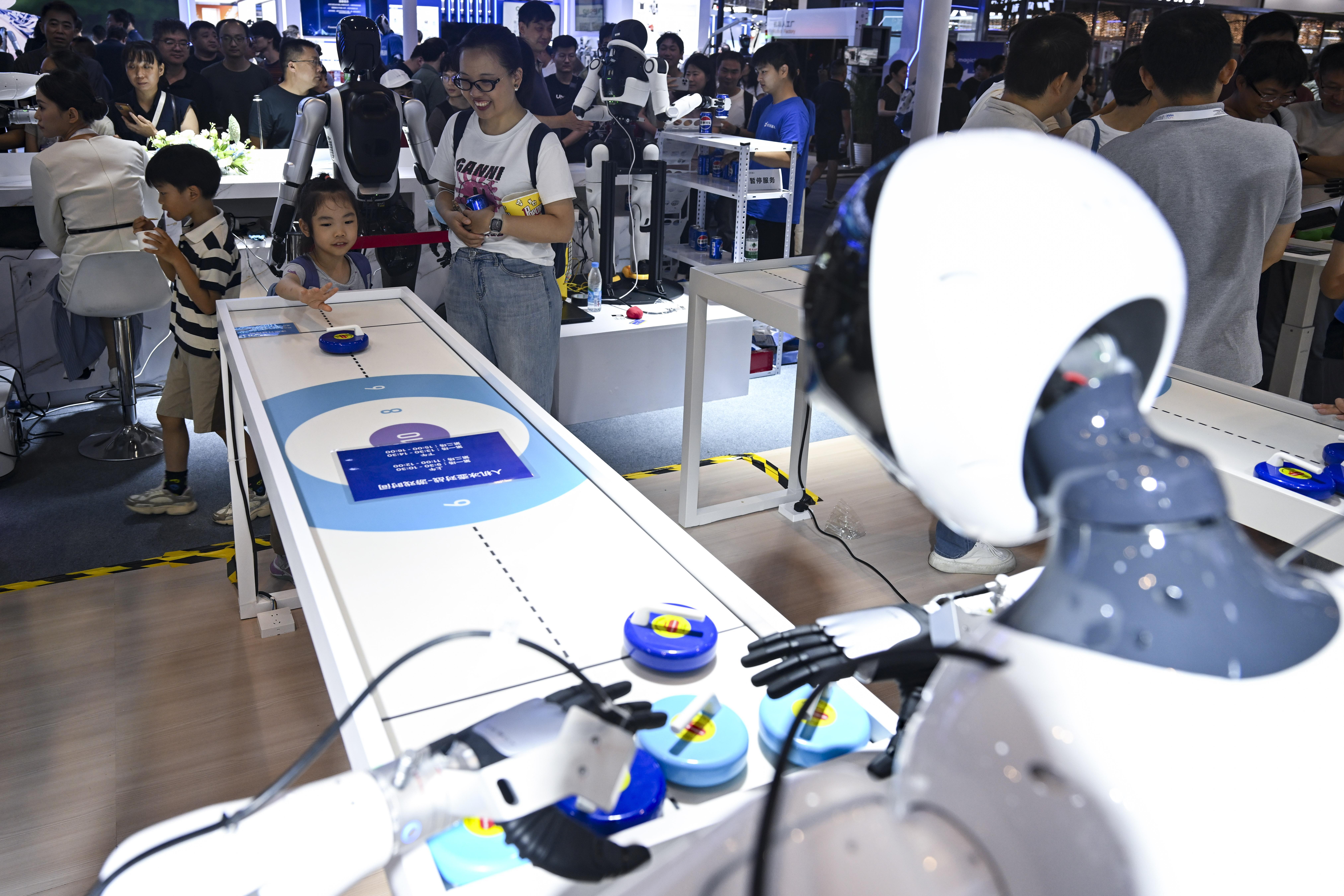  7月29日，小朋友在和一款机器人玩冰壶游戏。图/新华社